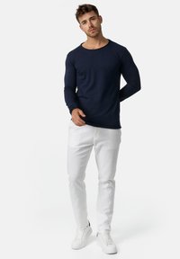 Marineblå langærmet skjorte med rund halsudskæring, parret med hvide slim-fit bukser og hvide sneakers, på en neutral baggrund.