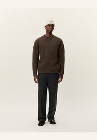 Ribbad brun tröja i kombination med mörkgrå vida byxor och en krämfärgad mössa med broderad text. Slät tyggtextur.
