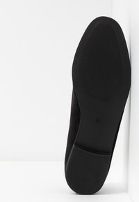Semelle de chaussure en daim noir avec grip en caoutchouc texturé. Design à bout rond et bord contouré. Surface lisse avec peu de détails.