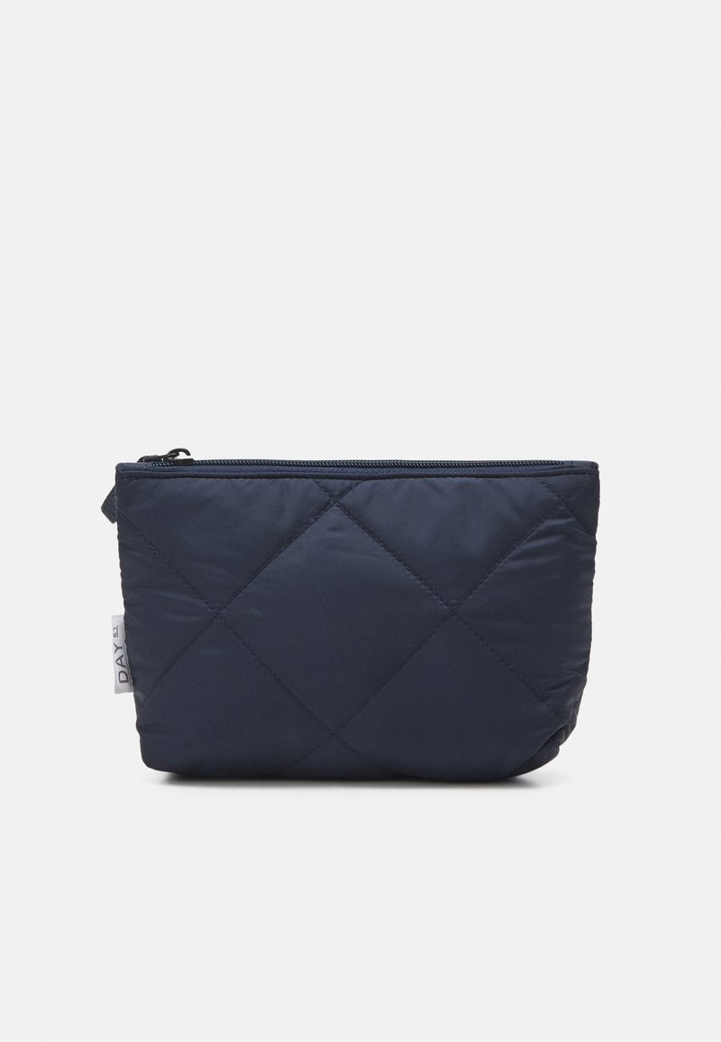 Bolsa acolchoada em azul-marinho, feita de tecido macio, com fecho em zíper e uma pequena etiqueta lateral. Forma retangular com padrões em diamante texturizados.