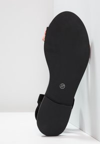 Black flat shoe sole with a smooth surface, featuring a size 37 label. A small, textured accent in a light color is visible at the heel.