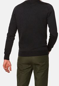 Suéter negro de manga larga en textura de punto suave, diseño ajustado, con puños y dobladillo acanalados, combinado con pantalones verde oliva.