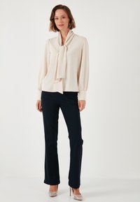 Light beige blouse with a bow tie at the neckline, long sleeves, and navy flared trousers, complemented by silver high-heeled shoes.
