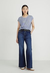 T-shirt à rayures à manches courtes en gris et marine, associé à un jean en denim foncé taille haute évasé, avec une ceinture noire et des chaussures blanches.