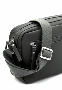 Borsa rettangolare nera realizzata in materiale liscio con tracolla in tessuto grigio. Presenta doppie cerniere e dettagli in hardware argentato.