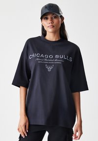 Černé oversized tričko s logem a nápisem "Chicago Bulls" bílé barvy, vyrobené z bavlny, s hladkou texturou a volným střihem.
