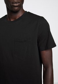 T-shirt in cotone nero con collo a giro e maniche corte, dotato di una tasca sul petto e una texture liscia.