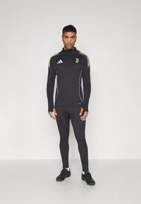 Black athletic tracksuit with zip collar, featuring yellow and light blue accents. Close-fitting leggings and black sneakers complete the outfit.