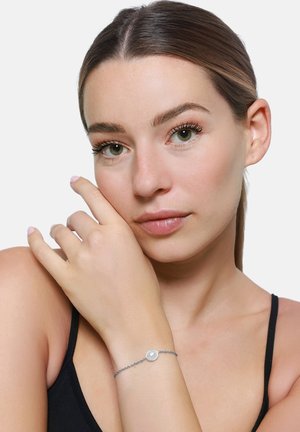 Bracciale in argento con accento di perla rotonda. Il design è minimalista, mettendo in mostra una texture delicata e una lucentezza sottile.