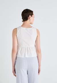 Top bianco senza maniche con dettaglio arricciato sul retro, realizzato in un tessuto leggero. Abbinato a pantaloni ricamati azzurri chiari.