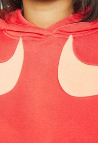 Röd hoodie i mjukt tyg, med stora beige lappar som ser ut som ögon. Inkluderar huva med dragsko och sydda detaljer.