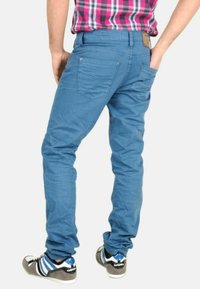Chinos de algodón azul con un ajuste slim, con una cinturilla plana, dos bolsillos traseros y una textura sutil. Combinados con zapatillas negras y azules.