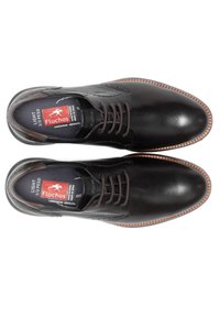 Zapatos de cuero negros con puntera redonda y cordones marrones, con una suela y etiqueta interior en contraste color tostado que exhibe la marca y un diseño ligero.