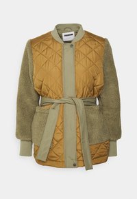 Vadderad brun jacka med olivgröna fleeceärmar, två stora framfickor, tryckknappar och ett matchande tygbälte knutet i midjan.