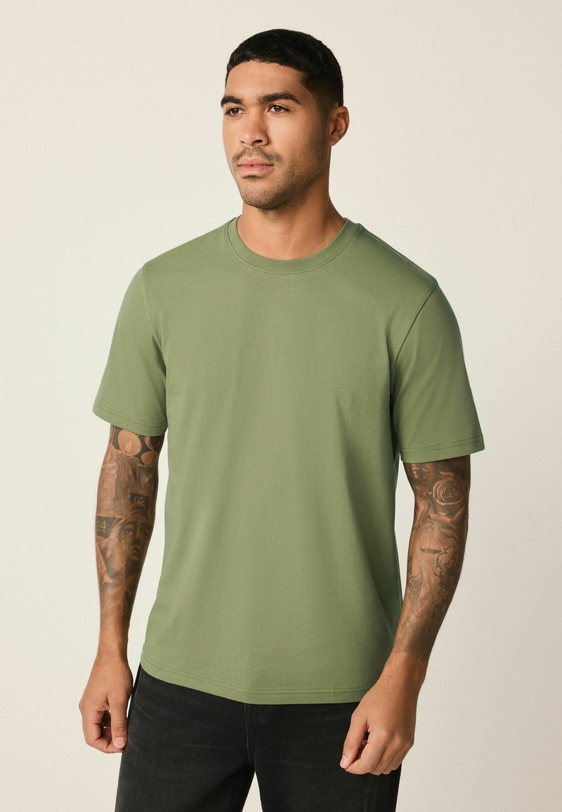 Zelena pamučna majica s okruglim izrezom, kratkim rukavima i ravnim rubom, s glatkom teksturom i ležernim krojem.