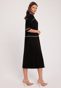 Czarna dzianinowa sukienka o średniej długości, z białymi akcentami na ciele i rękawach. Uzupełniona beżowymi szpilkami.