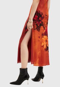 Rotes Blumenkleid mit hohem Schlitz, kombiniert mit schwarzen Leder-Ankle-Boots mit spitzer Zehenform und goldenen Akzenten an der Ferse.