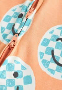 Hellorange Stoff mit blauen und weißen karierten Smiley-Gesichtsmustern. Verfügt über einen kontrastierenden Reißverschluss in Pfirsich. Weiche Textur.