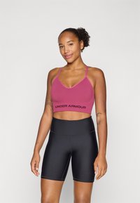 Magenta sportsbh med justerbare stropper og svart Under Armour-logo, sammen med høyt liv svarte sykkelshorts. Glatt, elastisk stoff.
