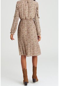 Robe fleurie en tissu doux et léger, avec manches longues et jupe plissée. Couleurs comprenant rose, vert et crème. Bottines marron à talons.