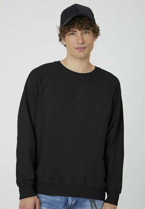 Black sweatshirt with a round neck, raglan sleeves, and ribbed cuffs. Worn with blue denim jeans. Simple, smooth texture.