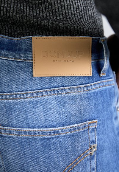 Blue denim jeans feature a leather patch with embossed text "DONdup Made in Italy" on the back. Standard stitching and pockets visible.