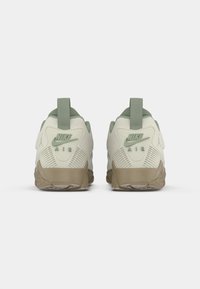 Pareja de zapatillas Nike Air en beige y verde vistas desde detrás, con mediasoles texturizados y tiradores en los talones.