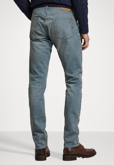 Heledad sinine denim pükste disain on lähedane, viis taskut ja nähtav logo detail tagumisel taskul. Kandmine pruunide saapadega.
