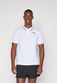 Hvit polo skjorte med stripete krage, korte ermer og en liten logo på brystet. Komplementert av svarte shorts.