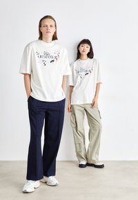 Hvide grafiske t-shirts med farverige splatter designs, iført med navy og oliven cargo bukser. Casual, afslappet pasform; blødt, åndbart stof.