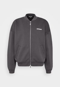 Dunkelgrau zip-up Bomberjacke mit einem gerippten Kragen, zwei Seitentaschen und weißem Logo auf der linken Brust. Glattes Material und lässige Passform.