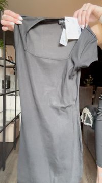 Abito grigio a maniche corte realizzato in tessuto morbido, con scollatura a barchetta e vestibilità ampia. Presenta un'etichetta attaccata al colletto.