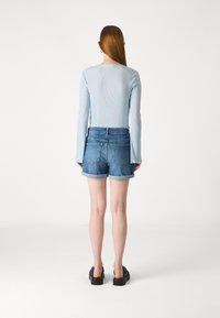 Maglietta a maniche lunghe a coste blu chiaro abbinata a pantaloni corti di jeans con orlo arrotolato. Le scarpe hanno una suola nera spessa. Design semplice e casual.