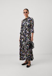 Lille lilledega maksimekko mustas kangas, värviliste mustritega, nööpide detailidega, kolmeveerandi varrukatega, koos mustade kingade ja tekstuurse käekotiga.