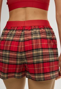 Rode geruite korte broek met een comfortabele elastische tailleband, gemaakt van een zachte, gestructureerde stof met contrasterende zwarte en beige ruitpatronen.