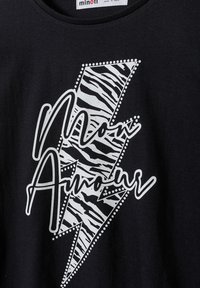 Crna pamučna majica s bijelim dizajnom munje u uzorku zebra, ukrašena točkicama nalik na studove i ručno napisanim tekstom.