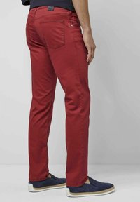 Rote Baumwollmischungshose mit schmalem Schnitt, zwei Gesäßtaschen und gestickten Details. Getragen mit navyfarbenen Slippers.