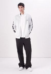 Svetlo siva jakna na zadrgo z mračnimi detajli, teksturirana tkanina in rebrast ovratnik, v kombinaciji z črnimi širokimi hlačami in belimi supergami.