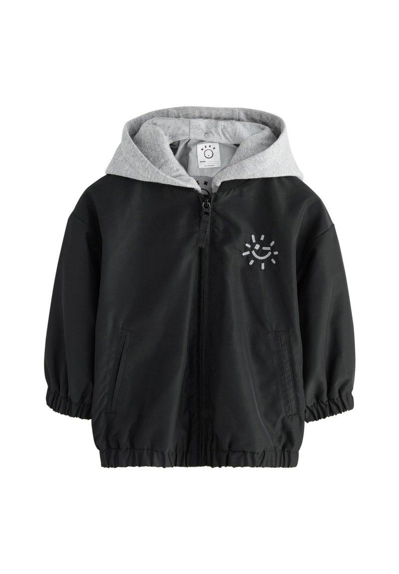 Veste légère noire avec capuche grise, poignets élastiques, fermeture éclair et poches avant. Présente un motif de soleil souriant sur la poitrine.