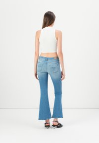 Blaue, auslaufende Jeans aus Denim mit mittelhohem Bund, mit einem verblassten Waschung, Gesäßtaschen und ausgefransten Säumen, kombiniert mit einem weißen Crop-Top.