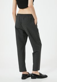 Zwarte pinstripe broeken met een elastische tailleband, zijzakken en taps toelopende benen. Gecombineerd met glanzende zwarte loafers.