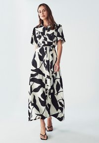 Maxi šaty s čierno-bielym listovým vzorom, krátkymi rukávmi, gombíkovým zapínaním vpredu a detailom opasku. Vyrobené z ľahkého materiálu.