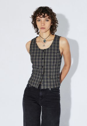 Sort-hvid ternet ærmeløs top med knapper foran, figursyet design og rund hals, kombineret med mørke jeans.