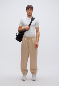 White athletic shirt with short sleeves, beige tapered sweatpants, and black crossbody bag. Model wears white sneakers. Simple, functional design.