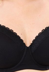 Svart bh med spetsdetaljer längs halslinjen, med en slät matt yta. Design med bygelförstärkning för stöd, sömlösa kupor med subtila detaljer.