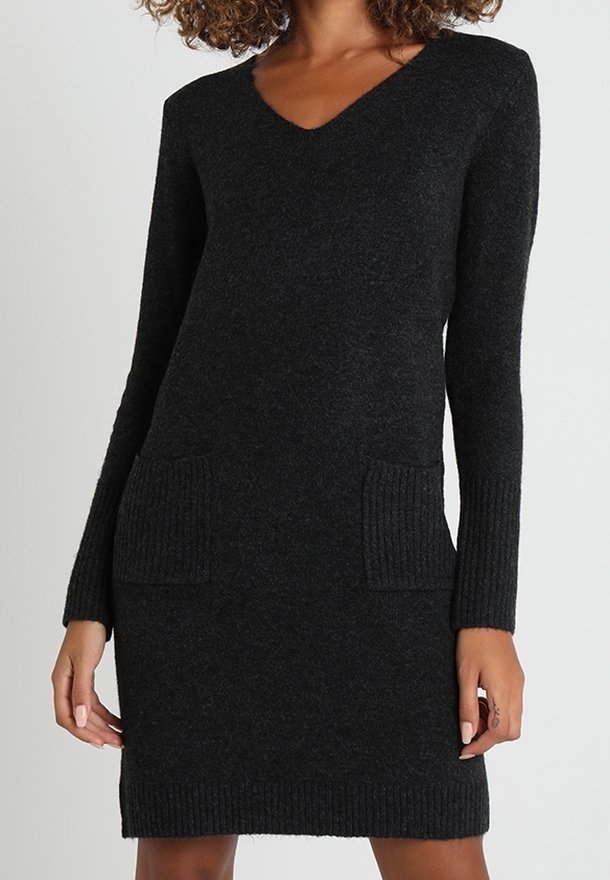 Robe noire en maille à manches longues avec col en V et deux poches côtelées sur le devant, portée par une personne aux cheveux bouclés.