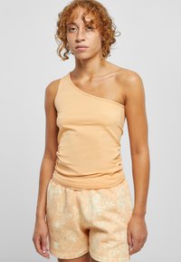 Éttetett, ensidig topp i myk ferskenfarget stoff, med rynkedetaljer ved midjen. Sammen med lette ferskenfargede shorts med blekkflekker.