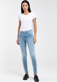 Vaqueros ajustados de color azul claro, hechos de denim, con una cintura a media altura, diseño entallado y sutiles bolsillos delanteros. Combinados con una camiseta blanca.