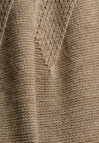 Gros plan d'un tissu beige tricoté avec un motif texturé présentant des côtes verticales et un détail en chevrons au centre.