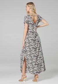 Maxikleid aus beigem Stoff mit schwarzen Zebra-Streifen. Es hat kurze Ärmel, einen tiefen V-Ausschnitt auf dem Rücken und seitliche Schlitze für zusätzliche Bewegungsfreiheit.